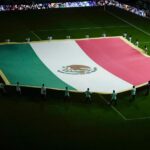 um grupo de torcedores mexicanos segura a bandeira do México no campo de futebol